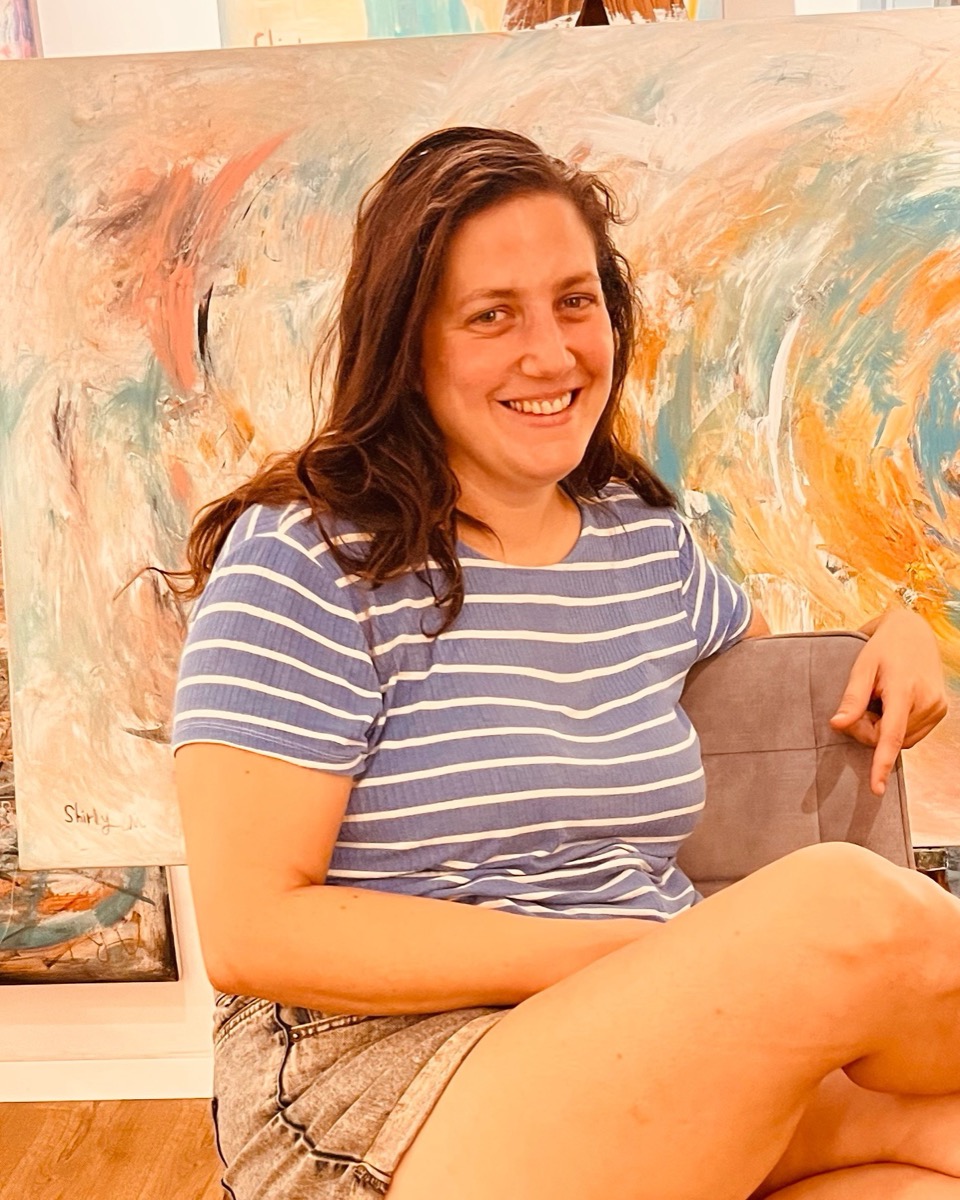 Merav Shaked in her studio, in front of one of her paintings