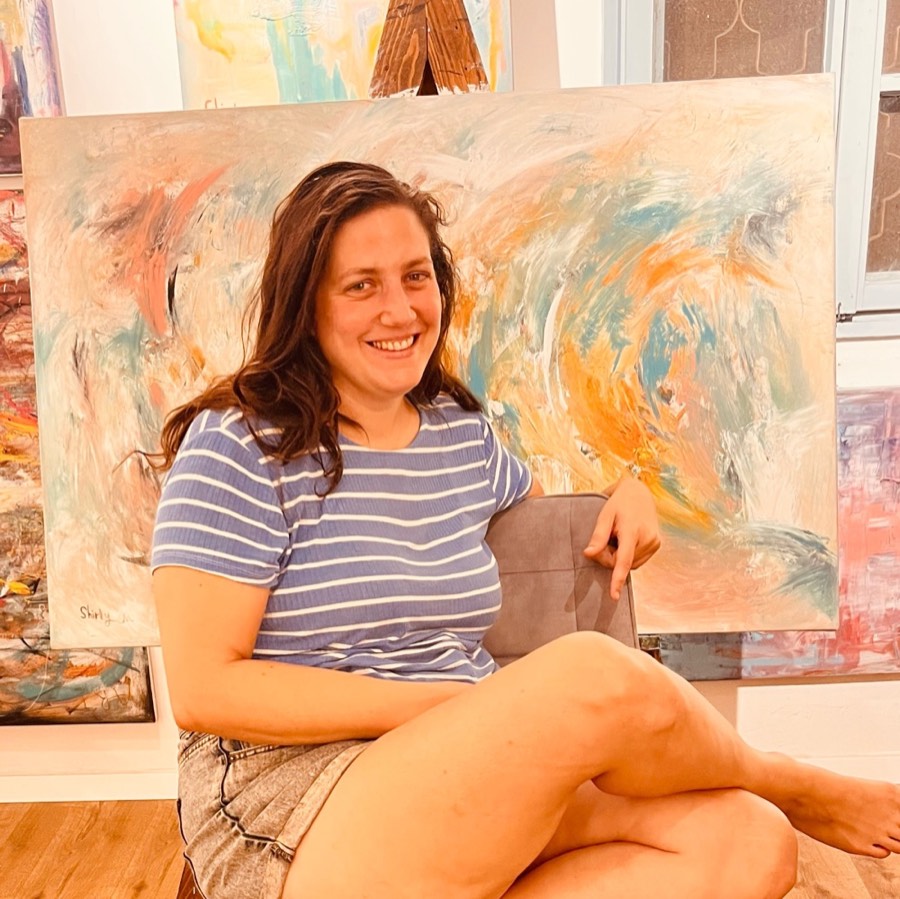 Merav Shaked sitting in her studio in front of large paintings