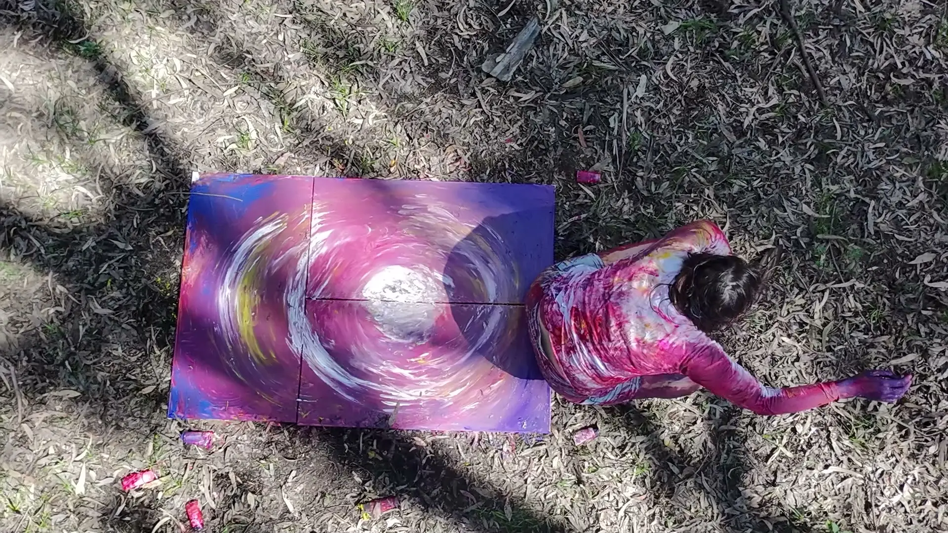 Merav, painted all over, crawling beside the canvas she painted with her body on the forest floor, drone shot