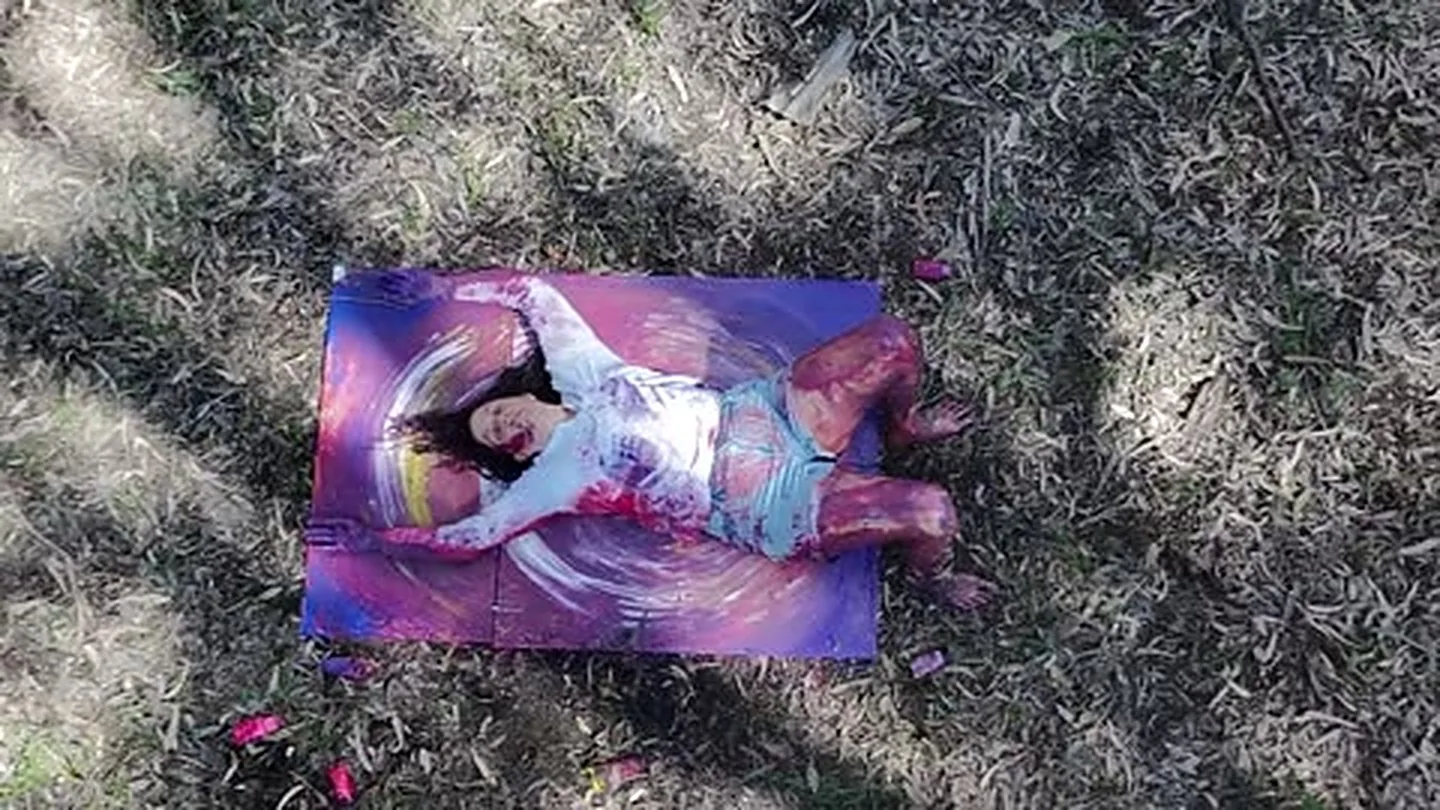 Merav Shaked creating with her body on a canvas laid in a field, seen from above