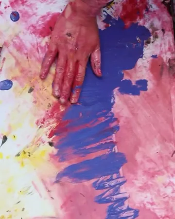 A hand covered in red paint resting on a blue and pink painting, from the Artidansel clip